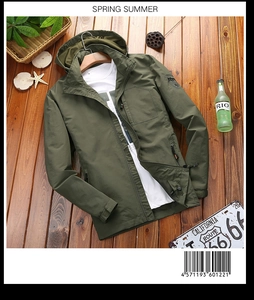 Detail of army green windbreaker featuring a chest zip pocket and sleeve badge on wood background