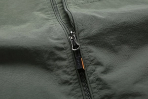Detail of olive green outdoor jacket with SPORTS branded zipper and orange accents