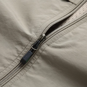 Detail of khaki outdoor vest showing metal zipper, sports puller, and breathable mesh lining