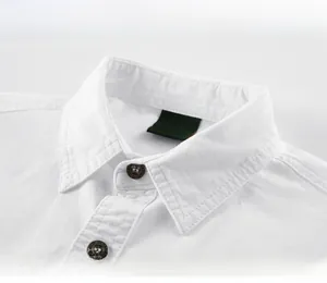 Dettaglio del colletto di camicia bianca con etichetta tessuta e logo ricamato in oro
