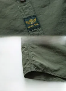 Detail view of woven logo label and curved hem on a dark green outdoor quick-dry shirt