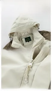 Detail of outdoor hooded jacket showing beige and brown contrast panels and metal zipper