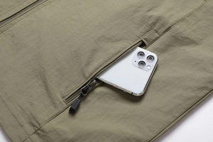 Detail view of olive green vest zip pocket holding a smartphone for storage scale