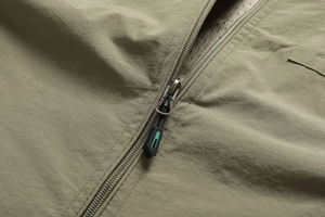 Close-up of olive green outdoor vest fabric with metal zipper and mesh lining