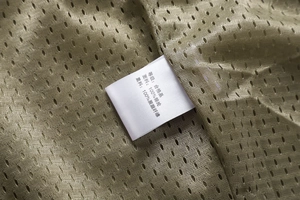 Detail of outdoor vest lining with olive green mesh fabric and wash care label showing material