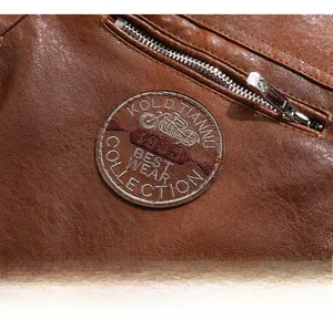 Detail of brown leather jacket featuring a vintage embroidered motorcycle patch and zipper