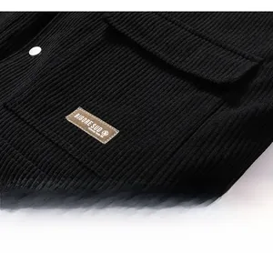 Close-up of black corduroy fabric texture with a brown brand tag and a silver metal button
