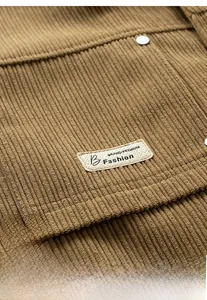 Macro shot of brown corduroy jacket detail with metallic button and woven logo patch