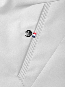 Close-up of a white utility jacket with a logo button and tricolor ribbon detail