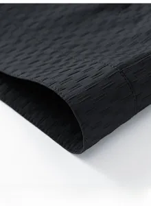 Detailed macro view of the black textured fabric with vertical pleats and straight hemline