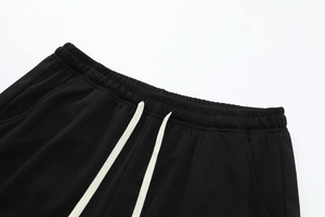 Detail of black athletic pants featuring elastic waistband and cream contrast drawstring
