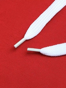 Détail de lacets plats blancs tissés avec ferrets clairs sur un fond rouge vif