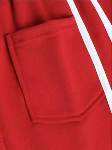 Détail du jogging rouge avec une poche carrée et des doubles bandes blanches latérales