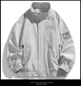 Detail of light gray outdoor jacket with stand collar and logo pocket on the sleeve