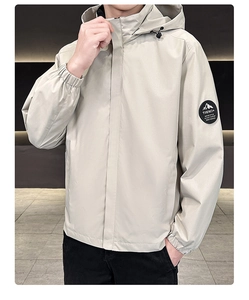 Detail view of the round mountain sleeve patch and adjustable drawstrings on a beige jacket