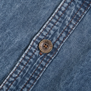 Macro shot of blue denim shirt showing orange double stitching and vintage metal button detail