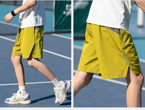 Detail of green sports shorts with reflective strip and side slit on a blue tennis court