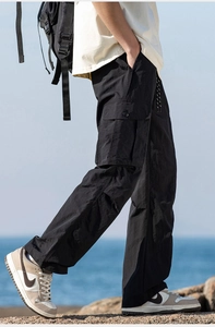 Detail of black technical cargo pants with large side pockets on coastal rocks