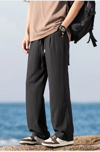 Close-up of black hiking pants with drawstring and rivet detail against seaside rocks