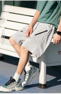Detail of light grey cargo shorts showing black zipper pocket and technical fabric texture