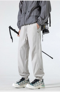 Detail of grey outdoor cargo pants featuring an elastic drawstring waist and zippered side pocket