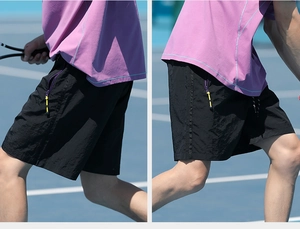 Detail of black sporty shorts showing zipper pocket with purple trim and yellow puller