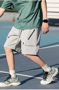 Detail of light gray cargo shorts with zipper pockets and drawstring on tennis court