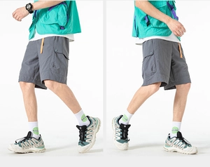 Detail view of grey cargo shorts featuring orange drawstrings and large snap-button side pockets