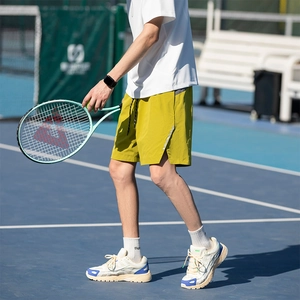 Mustard yellow men's sports shorts with reflective stripes and drawstring in a tennis court