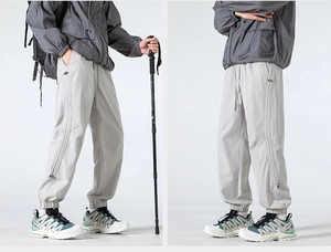 Detail of light gray outdoor techwear pants with adjustable drawstring and side zippers