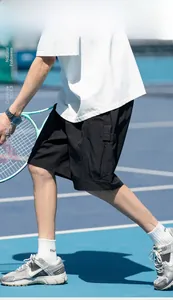 Streetwear style black cargo shorts with large flap pockets on a blue tennis court