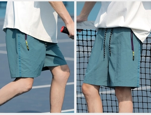 Detail of blue-green athletic shorts featuring contrast drawstrings and functional zip pockets