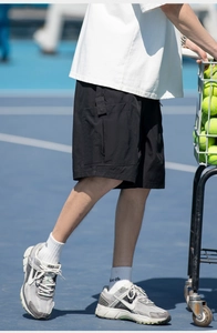 Dynamic detail shot of black cargo shorts with flap pockets on a tennis court