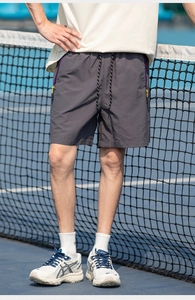 Men's dark grey quick-dry sports shorts with yellow zipper pocket at tennis court