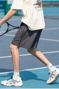 Detail of charcoal grey quick-dry shorts with yellow zipper pull on blue tennis court