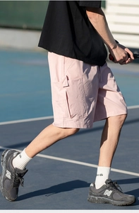 Detailed outdoor shot of light pink cargo shorts with side flap pockets on a sports track