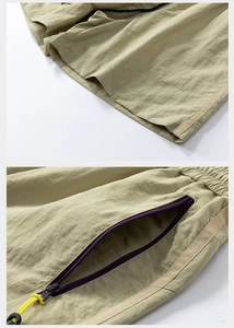 Detail of khaki cargo shorts showing the zipper pocket with yellow pull cord and durable fabric