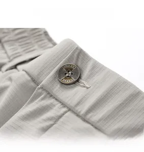 Detailed close-up of light gray trousers with elastic waistband and engraved metal button