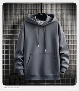 Detail of grey hoodie showing kangaroo pocket and drawstring on industrial grid wall