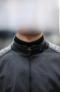Detail of men's black faux leather biker jacket featuring a stand collar and quilted shoulders