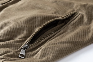 Macro detail of men's brown jacket featuring waffle texture fabric and metal zipper pocket