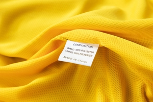 Detail of breathable yellow polyester fabric with mesh texture and care label on the jacket
