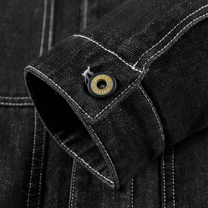 Gros plan du poignet d'une veste en jean noire avec coutures blanches et bouton en métal