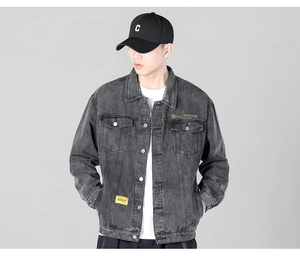 Detail of grey washed denim jacket featuring gold chest embroidery and casual styling