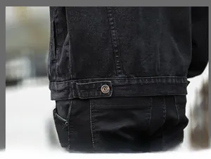 Detailed close-up of dark grey denim jacket hem with adjustable metal button and stitching