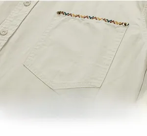 Close-up of beige cotton shirt pocket with ethnic embroidery and metal rivets detail