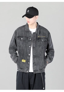Detailed view of dark grey washed denim jacket with yellow embroidery and flap pockets
