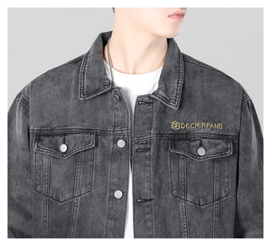 Detail of grey washed denim jacket featuring yellow chest embroidery and metal buttons