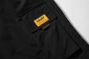 Detail of cargo pocket featuring yellow brand label on black durable fabric texture