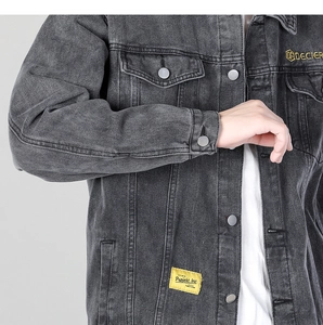 Detail shot of vintage grey denim jacket showing chest pocket and yellow embroidery